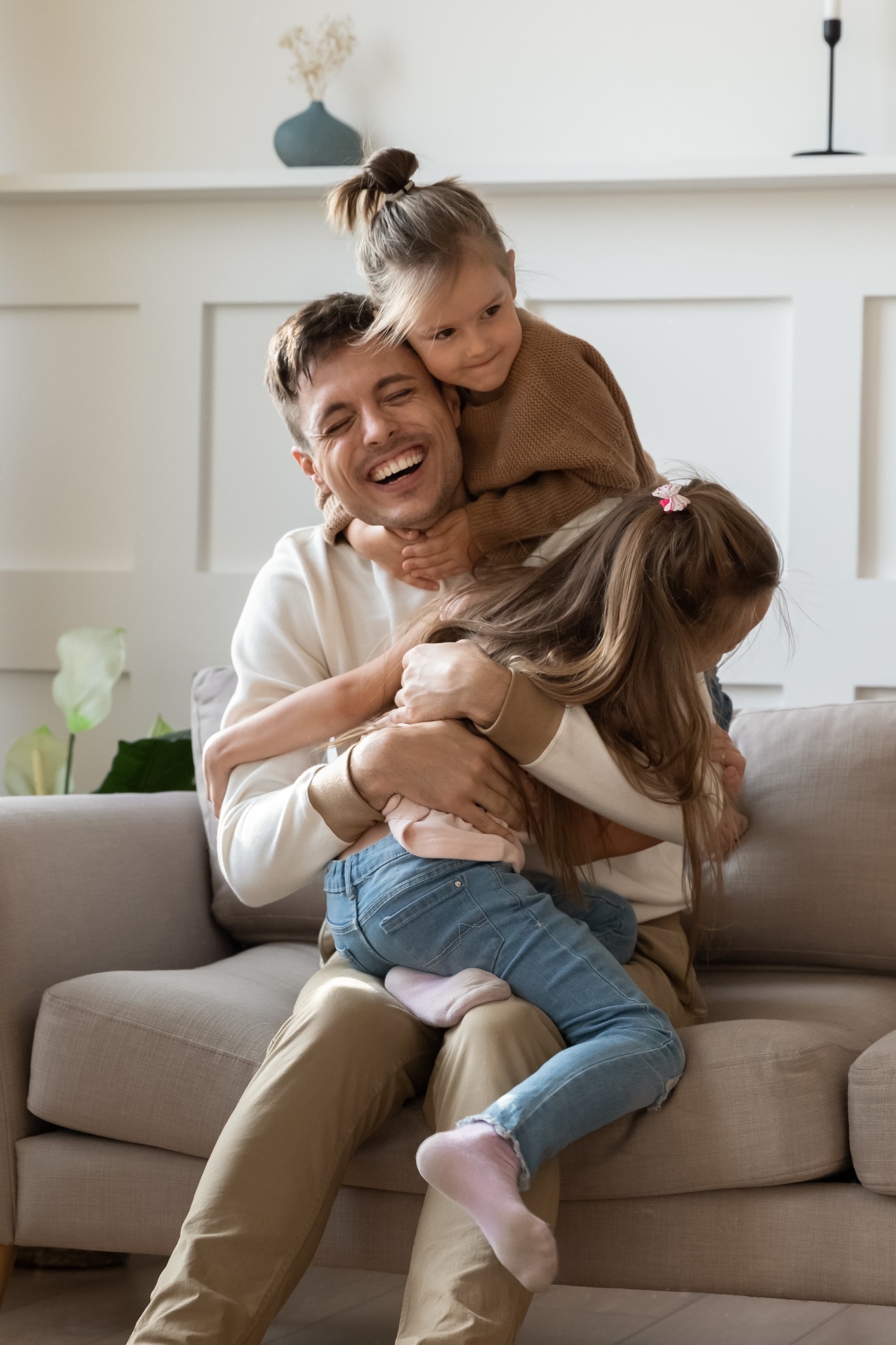 A man laughing on a sofa with two young girls hugging him