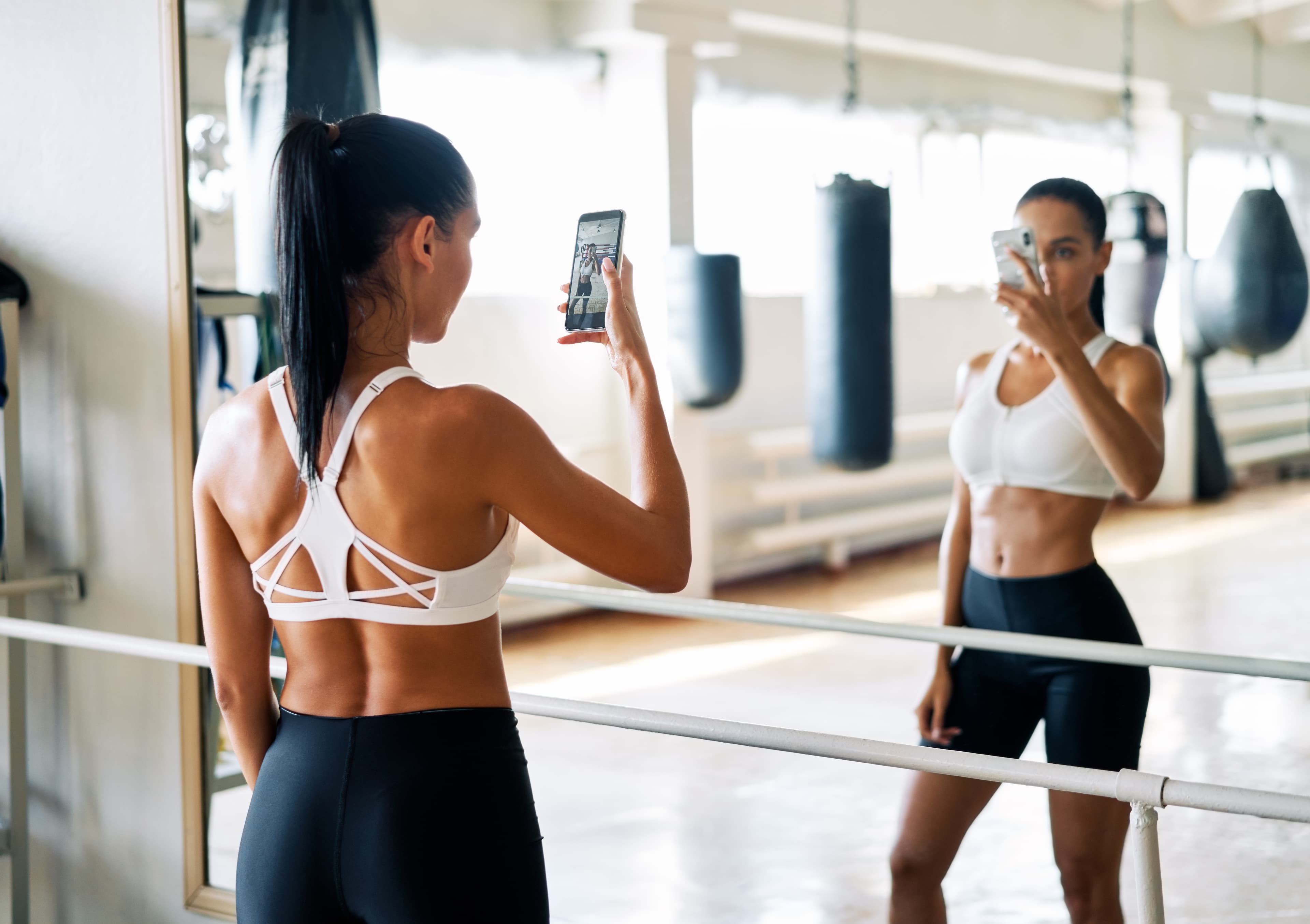 A woman in gym clothes taking a photo in a training studio mirror