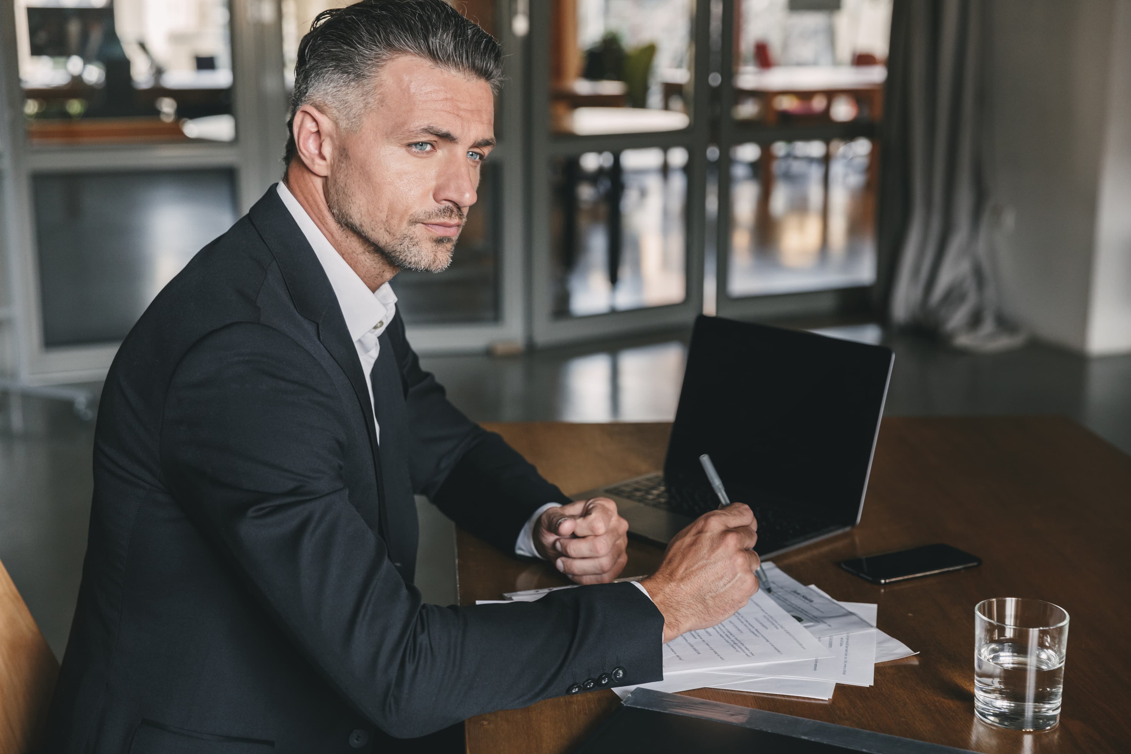 A man in a suit working at a table with a laptop and papers