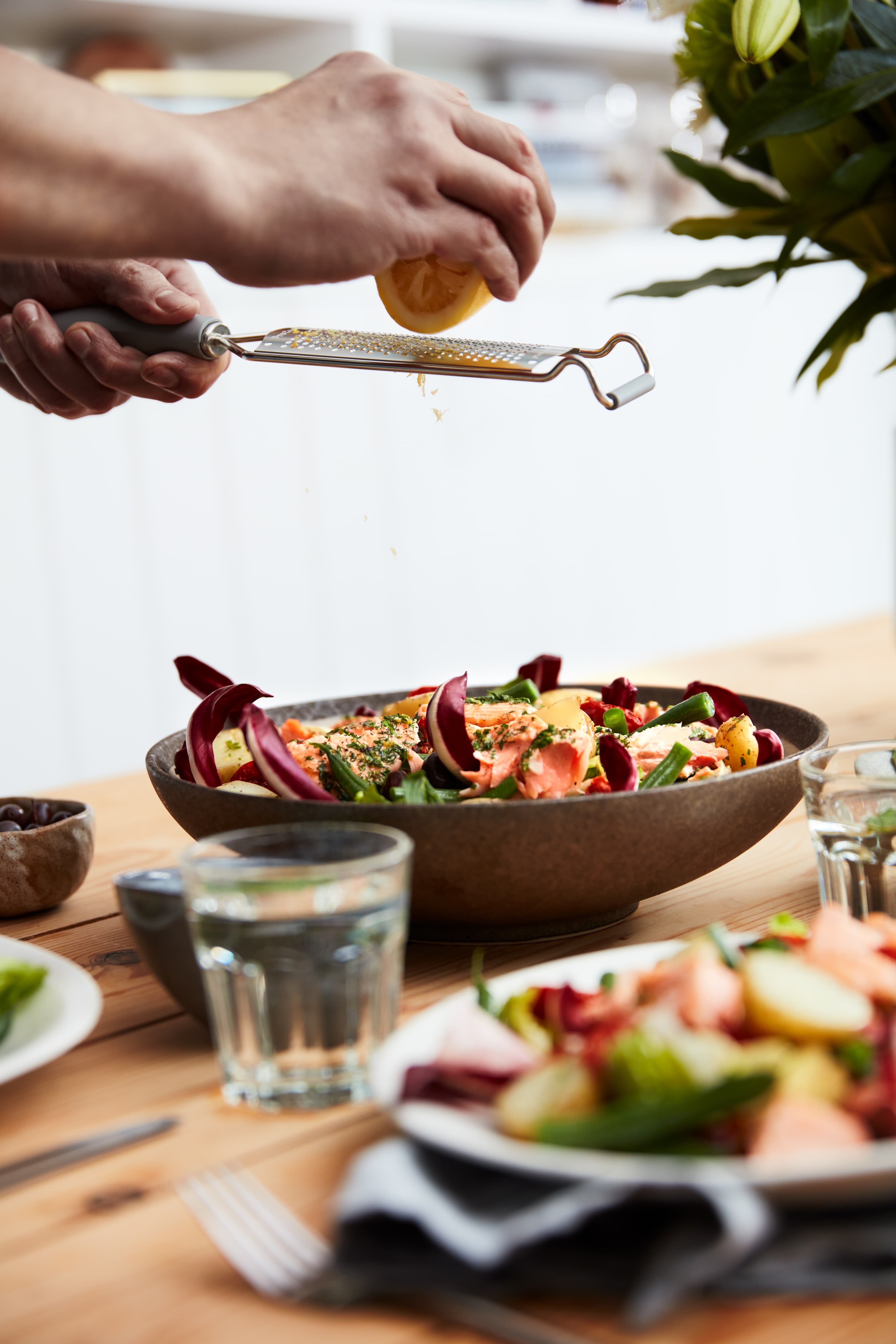 A chef zesting lemon over a bowl of salmon, new potatoes and radicchio at a laid table