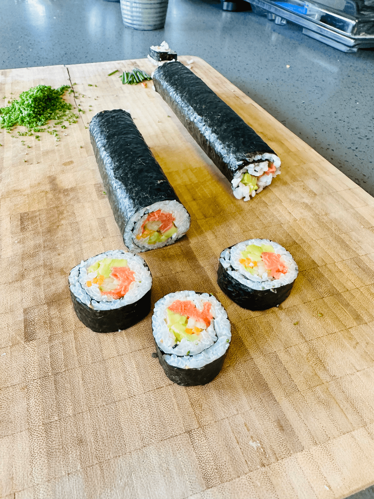 Two seaweed-wrapped rice rolls on a wooden board, with four cut pieces showing salmon, egg and vegetable filling