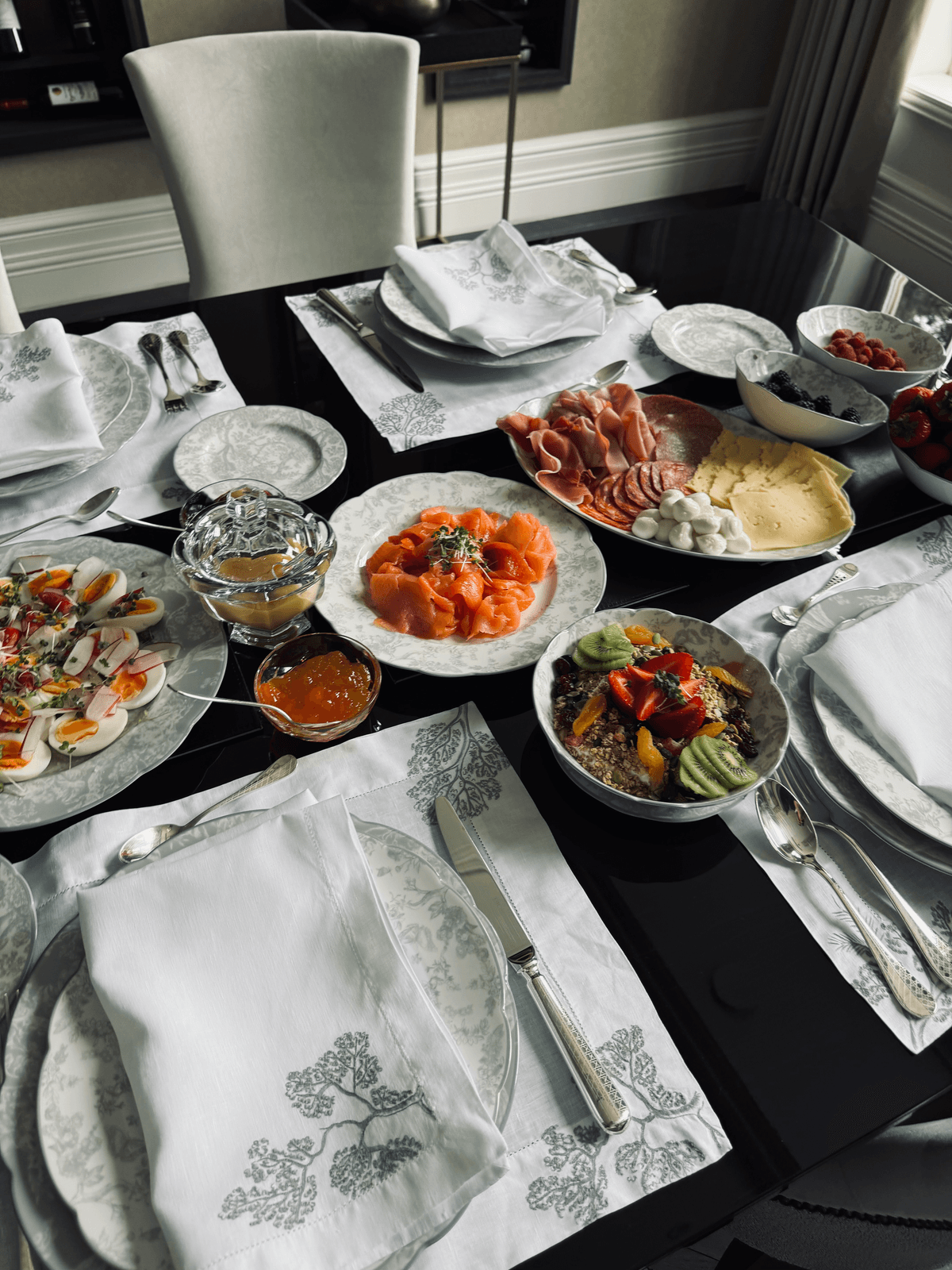 A table laid with sharing plates of cured meats, smoked salmon, vegetables and dips, with linen napkins and cutlery