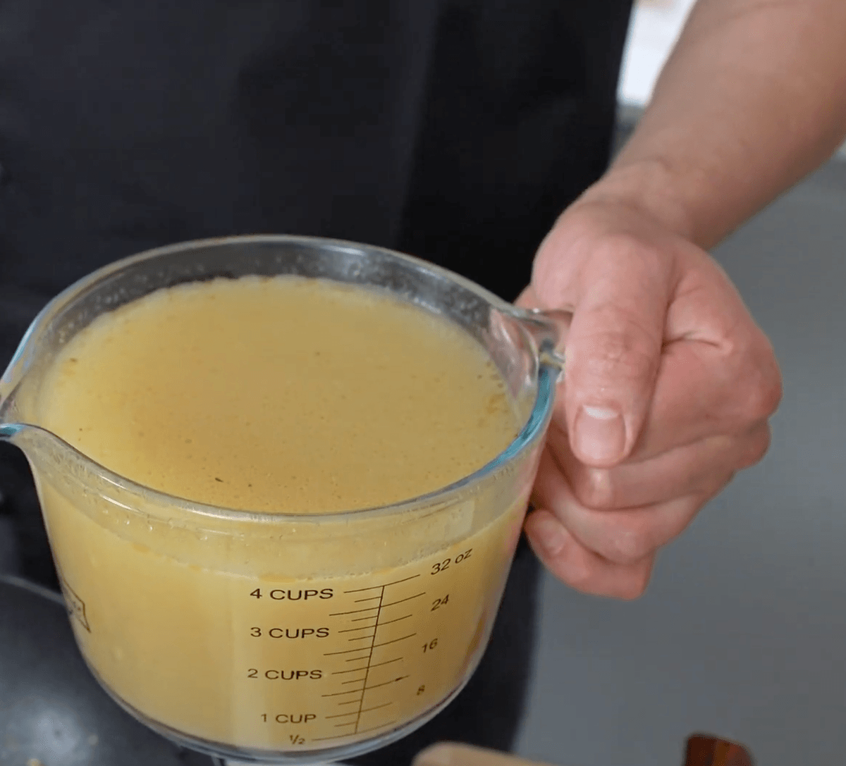 A chef holding a glass measuring jug filled with pale broth