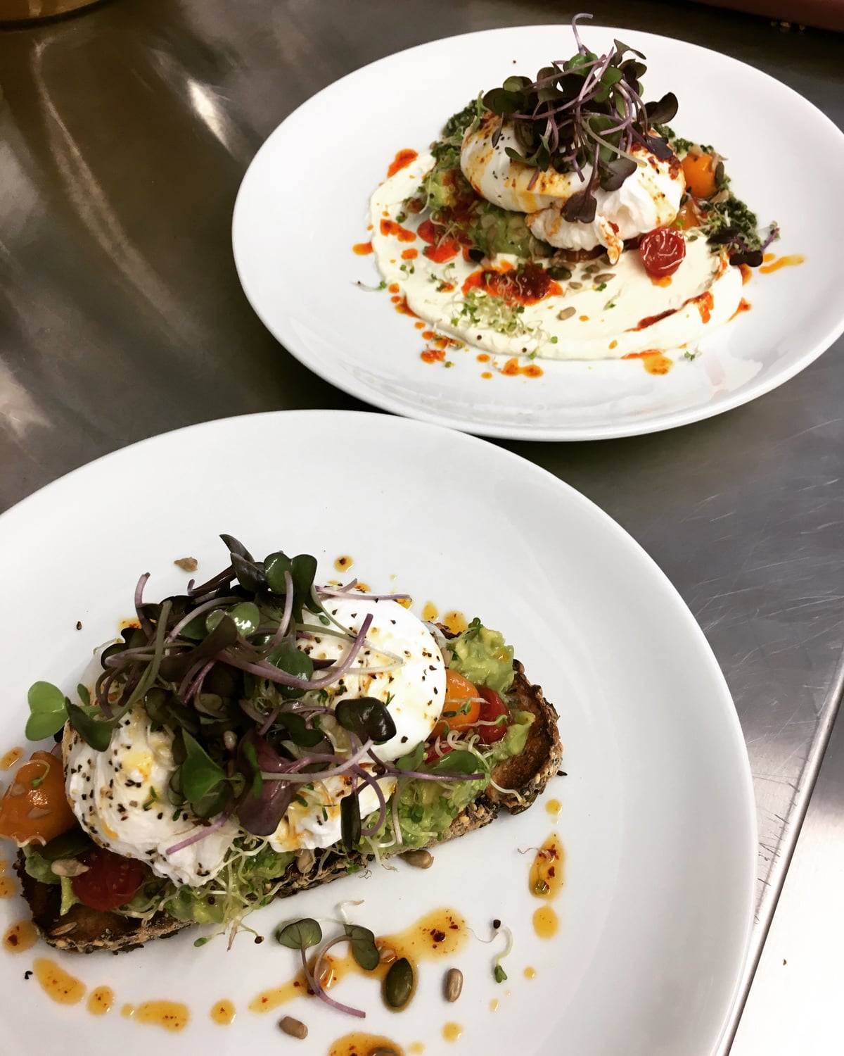 Two plates: poached eggs with prawns and herbs, and avocado on toast with a poached egg and microgreens