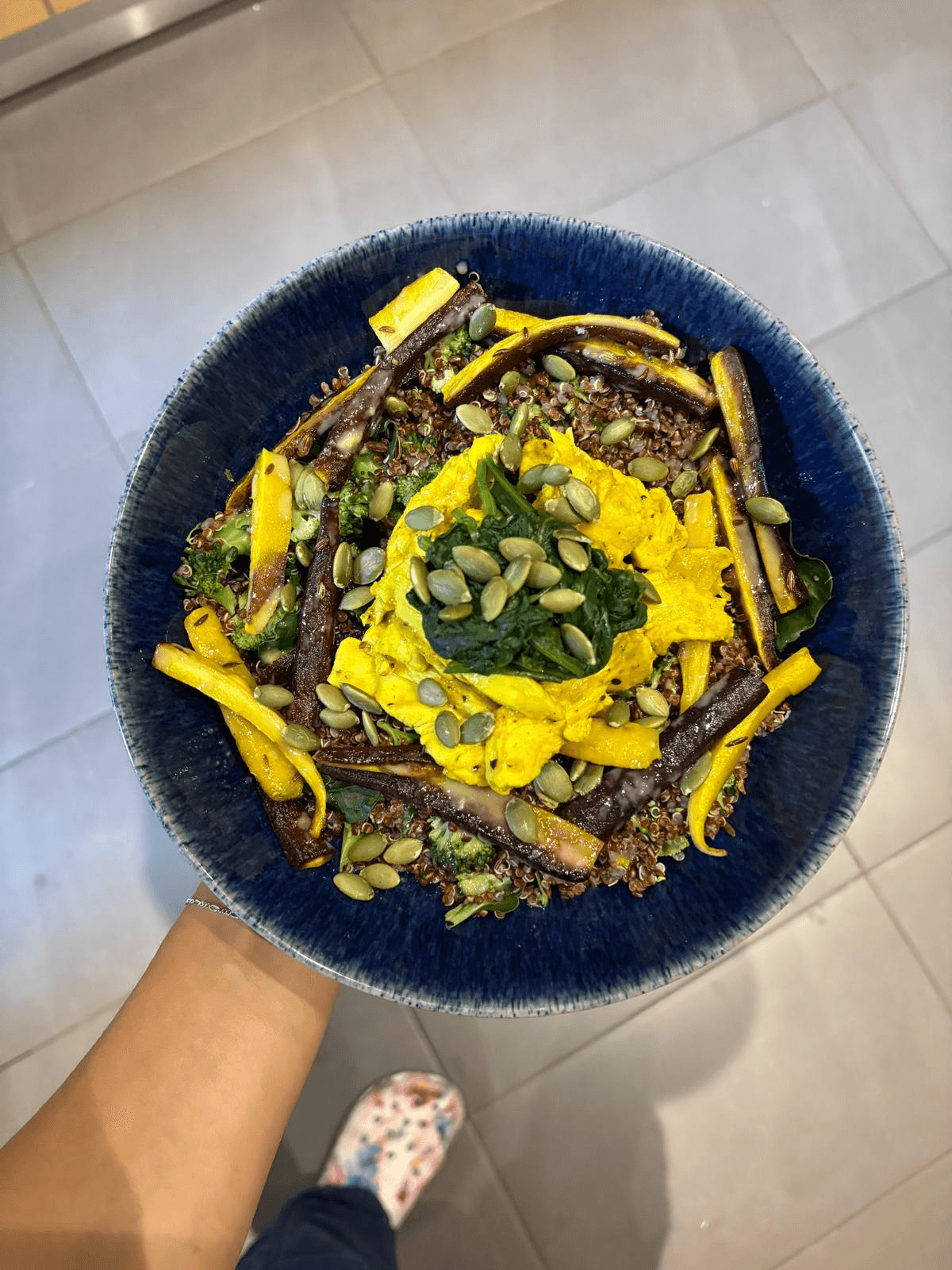 A dark blue bowl of a lentil and grain dish topped with turmeric sauce, pumpkin seeds and herbs