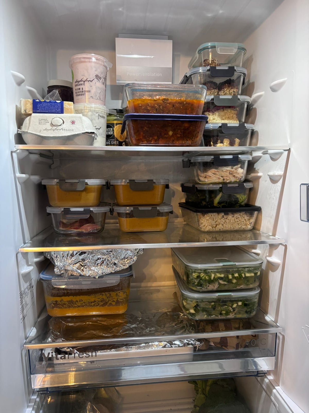 An open fridge stacked with labelled glass containers of prepared meals