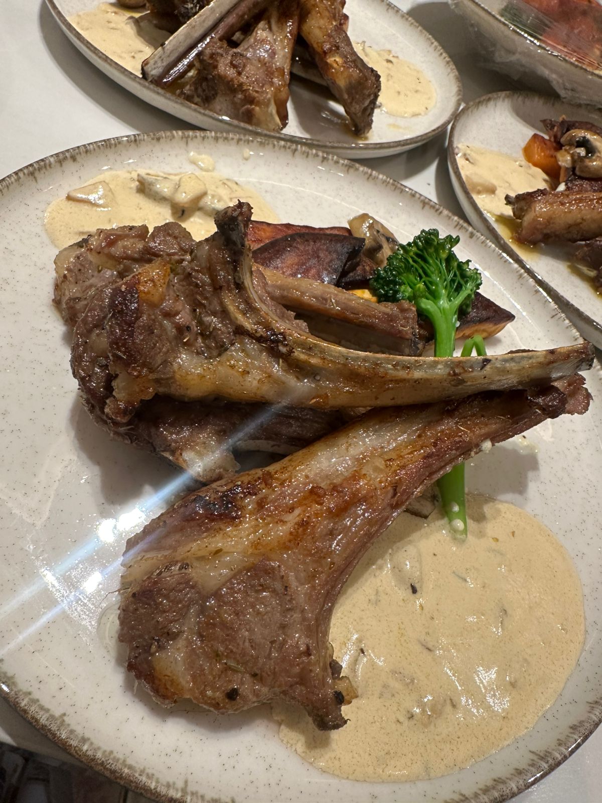 Lamb chops served with a creamy sauce and tenderstem broccoli on a stoneware plate