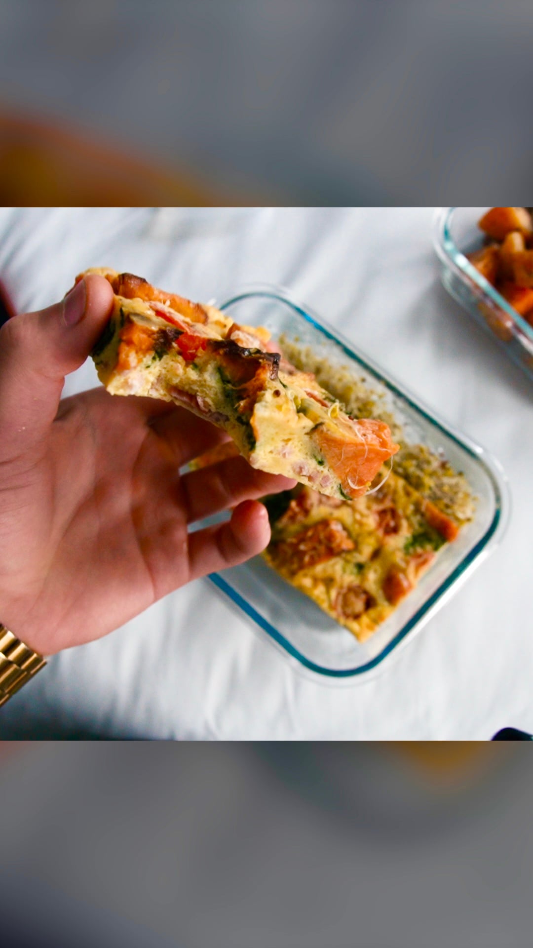 A hand lifting a slice of baked egg and vegetable tart out of a glass dish