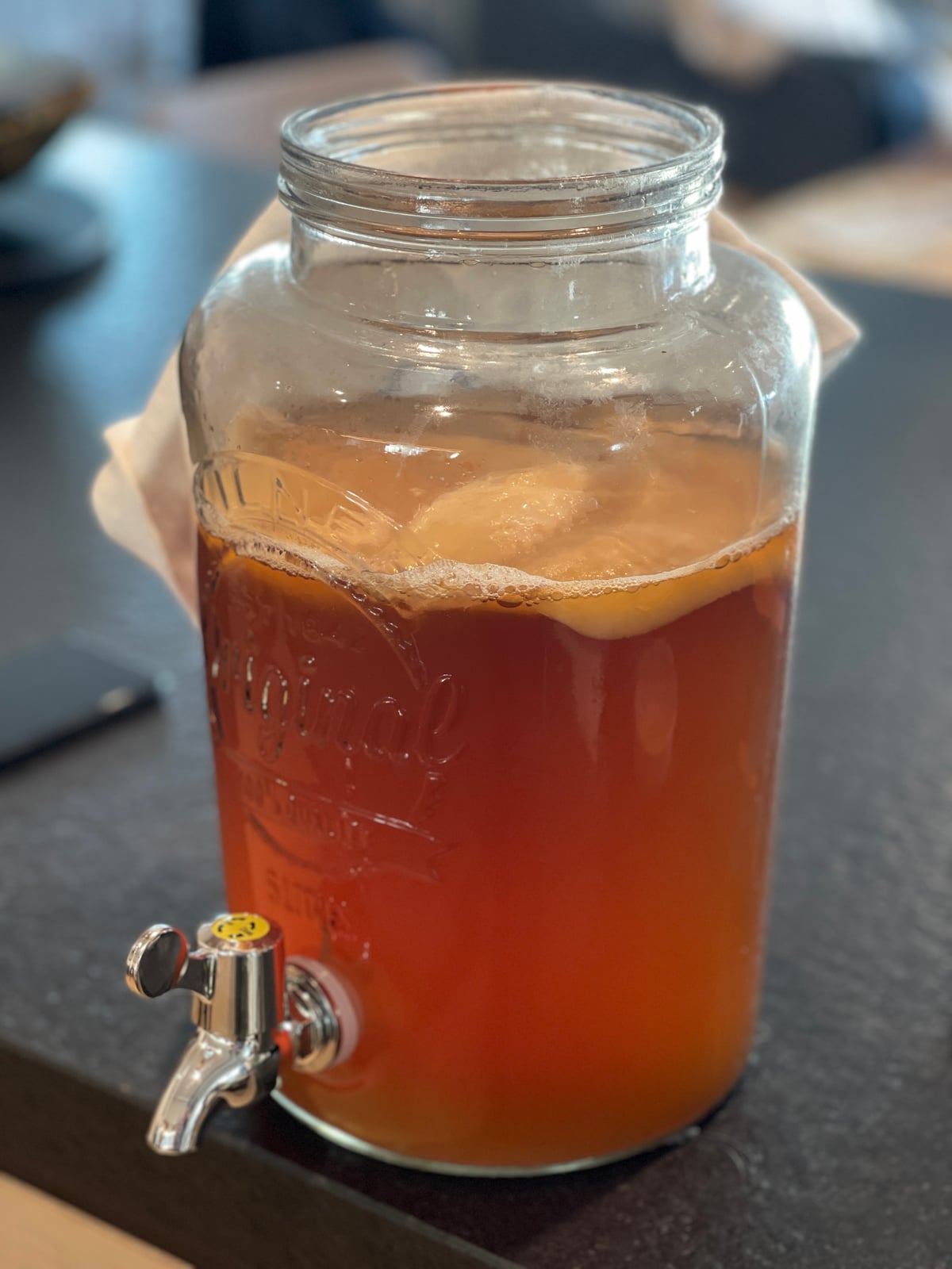 A glass dispenser jar of amber fermented tea with a tap