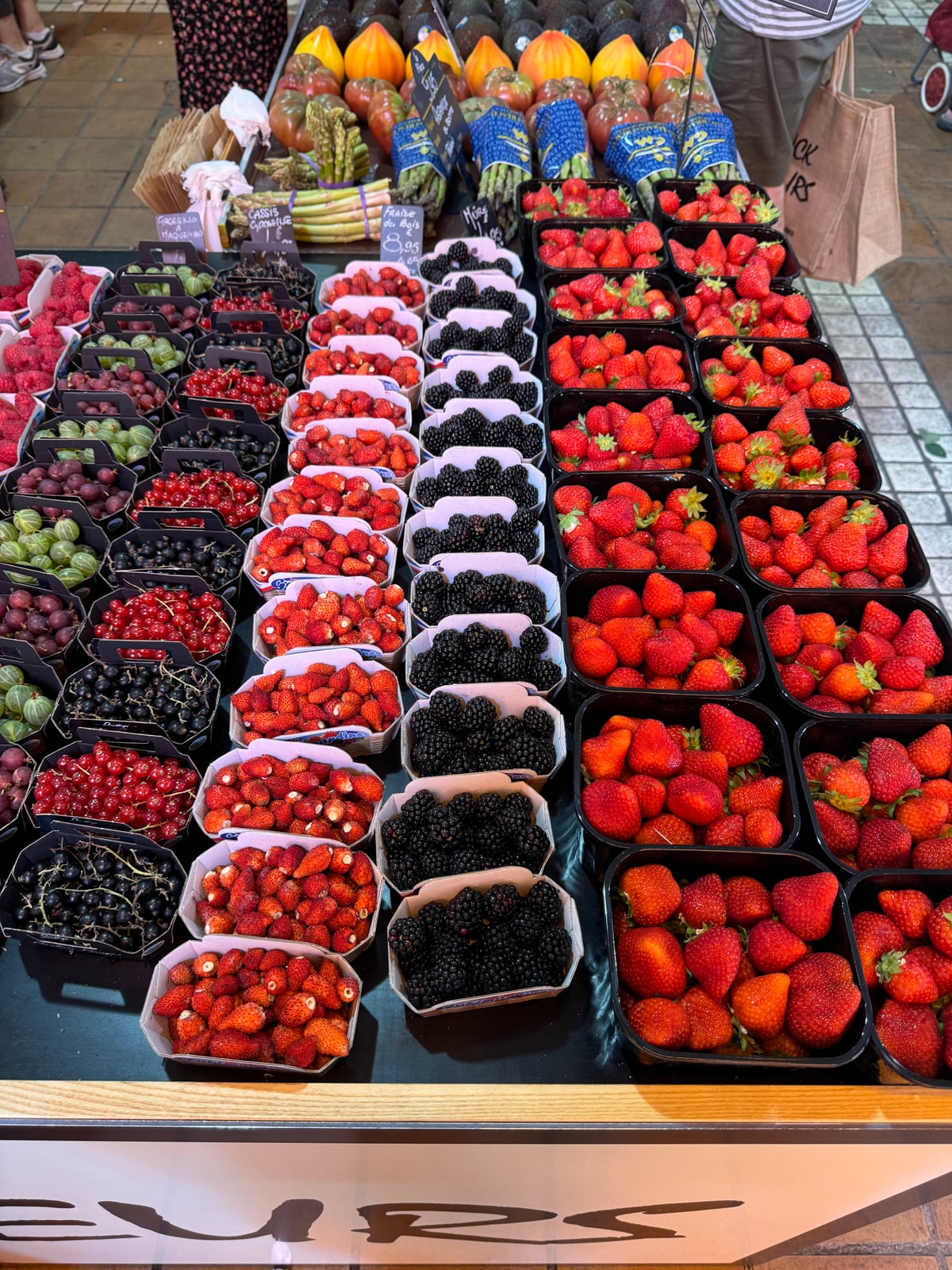 A market stall laid out with punnets of strawberries, raspberries, blackberries, redcurrants, blackcurrants and gooseberries, with tomatoes and asparagus behind